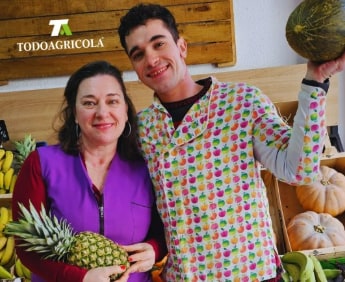 El equipo de Todo Agrícola en la tienda, bajo el rótulo, con una piña y un melón